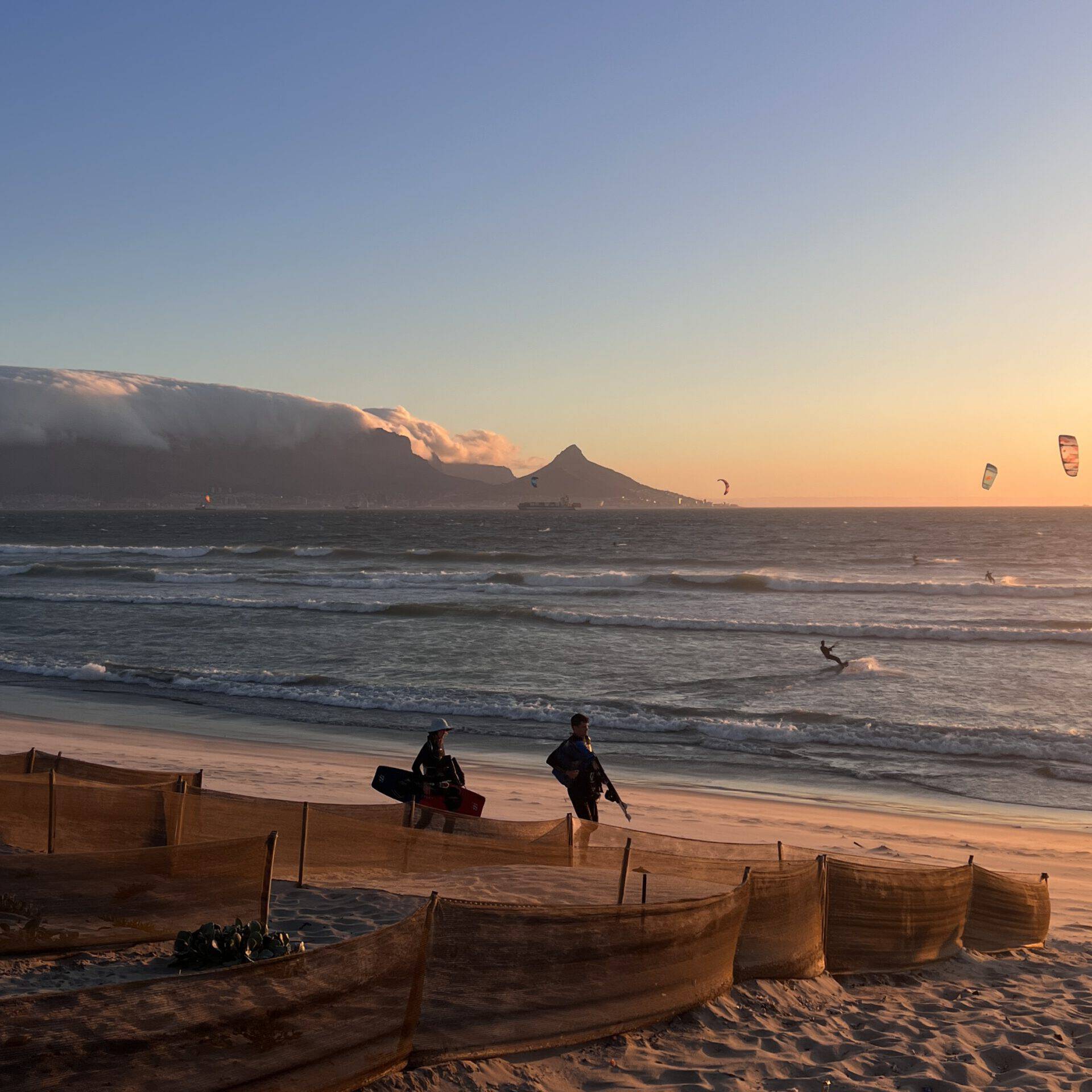 Kitesurfers on Bloubergstrand Beach at sunset near Cape Town Surfers Lodge with Table Mountain and Lion's Head in the background.