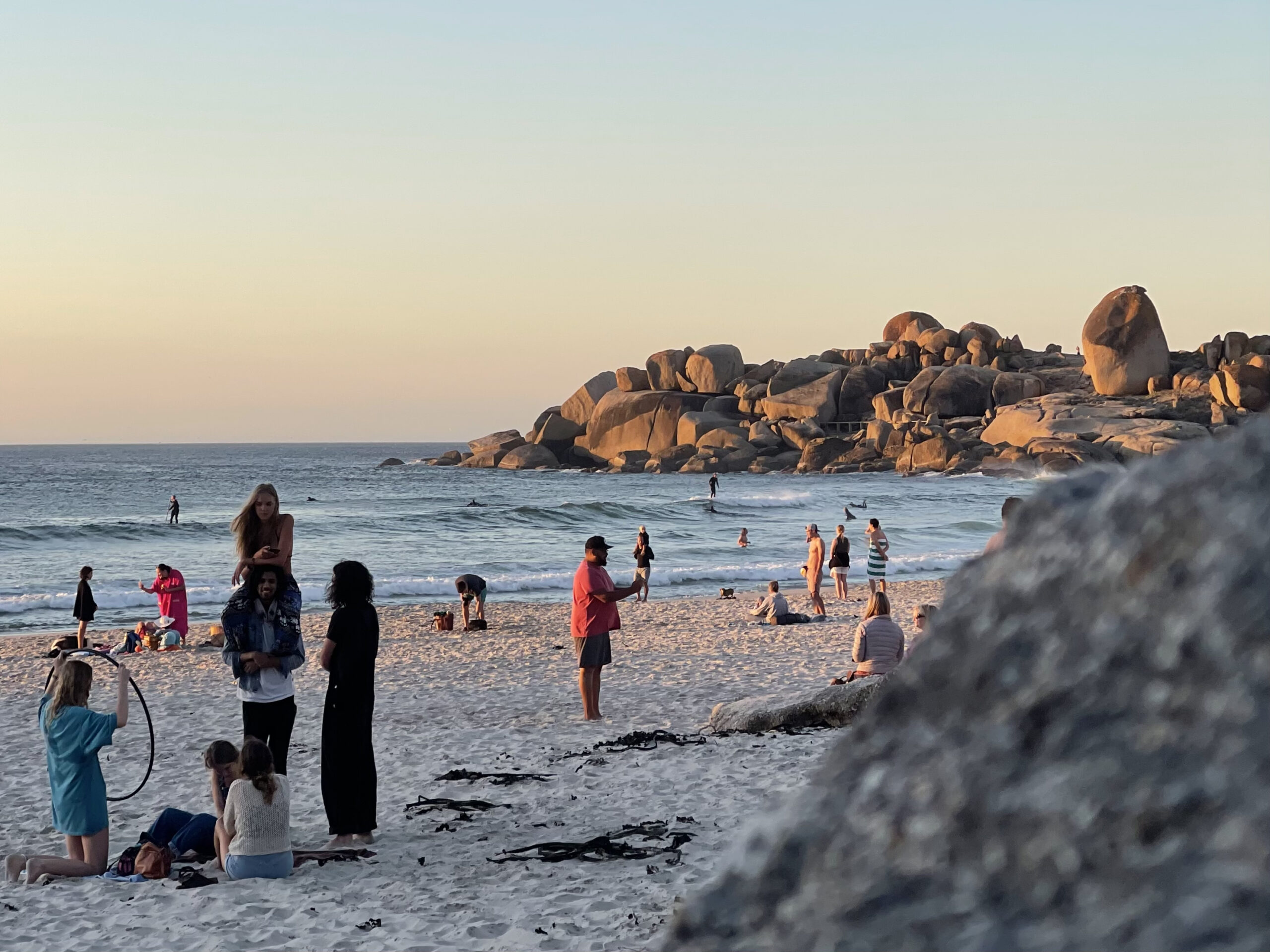 People enjoying Llandudno Beach at sunset, with large rock formations in the background and a golden glow from the setting sun.