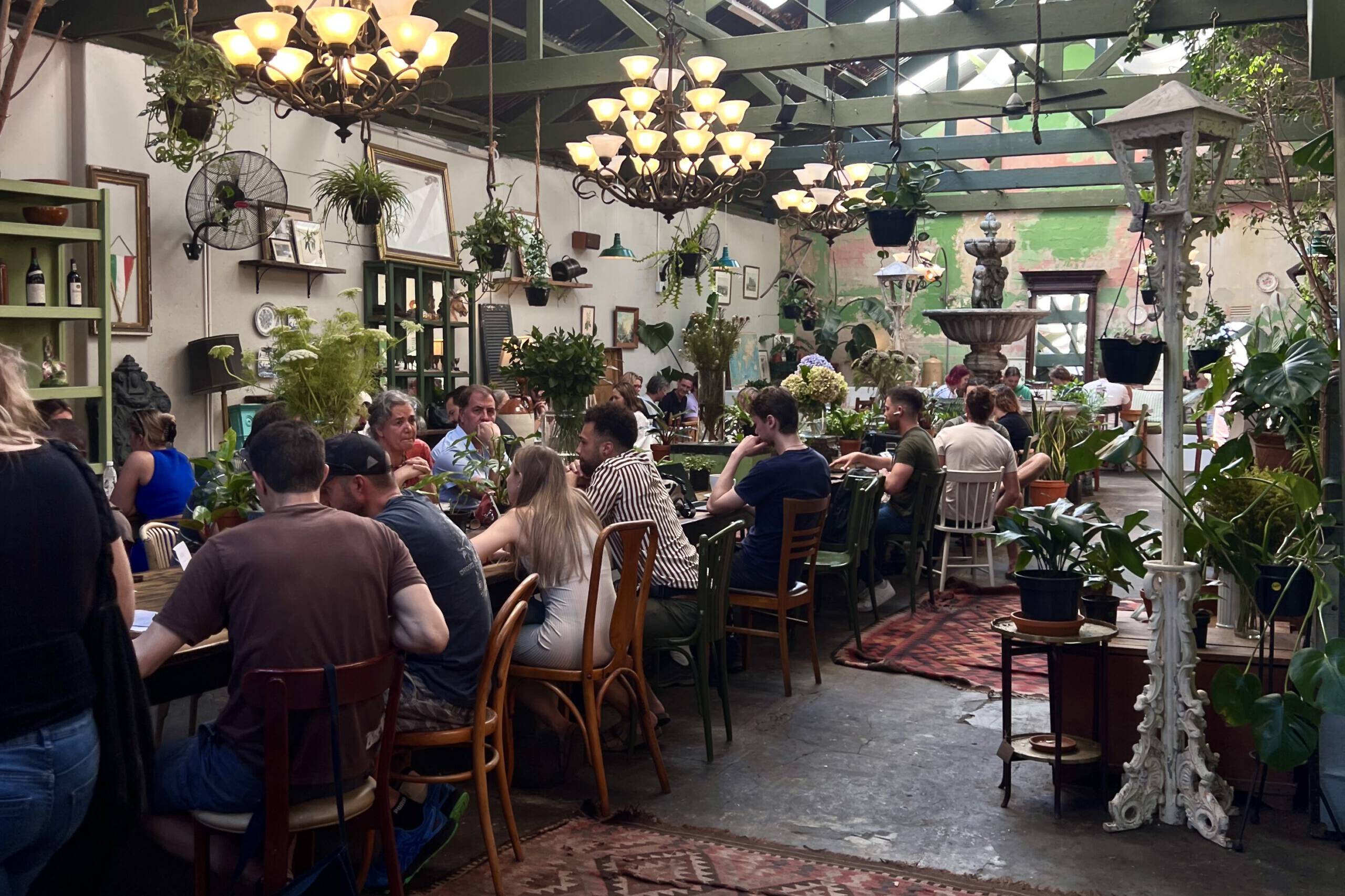 People enjoying a charming café in the city centre of Cape Town, surrounded by greenery and eclectic décor with a central fountain.