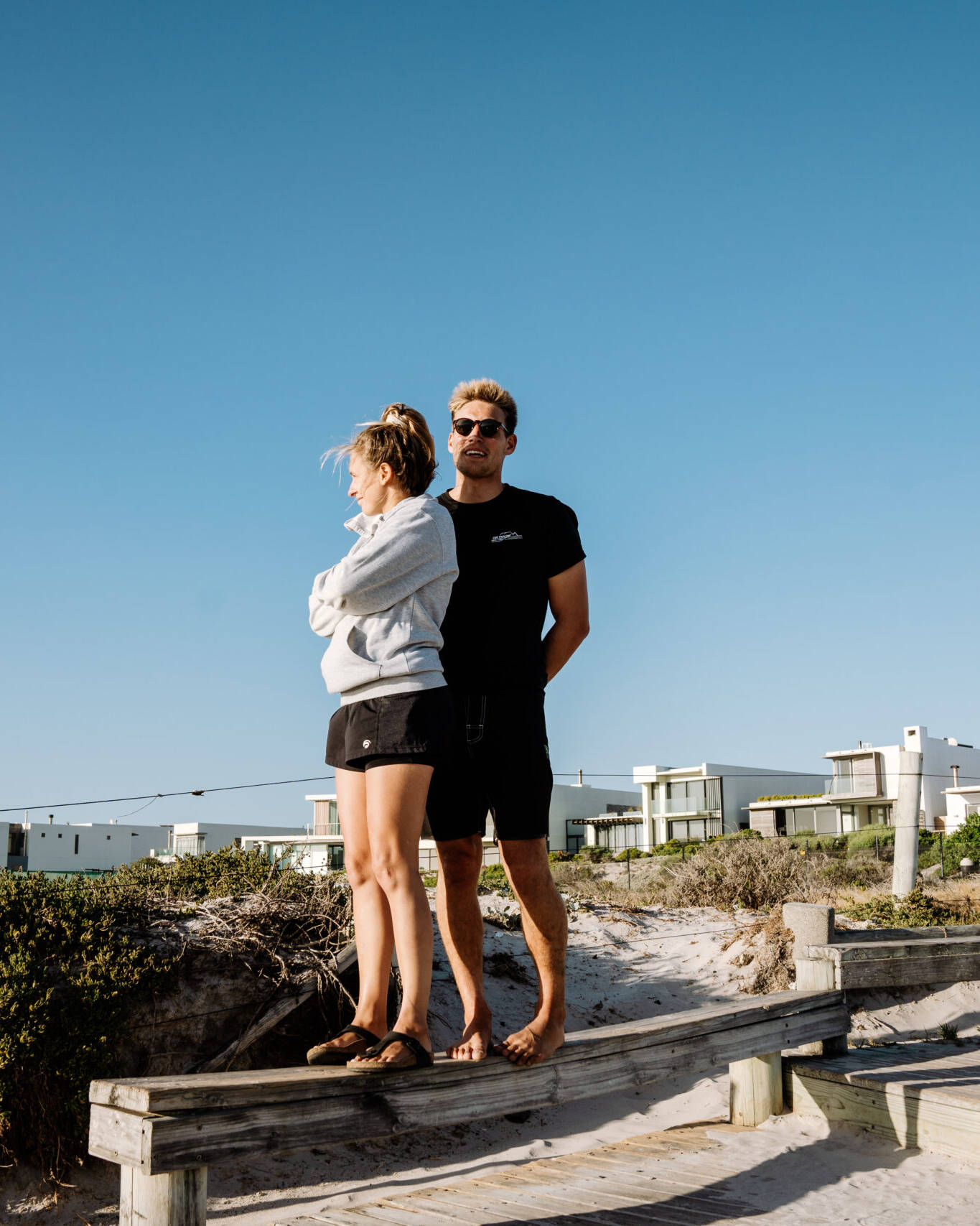 Two kitesurfer standing on a wooden platform at a beach in Big Bay, Cape Town, checking the conditions.