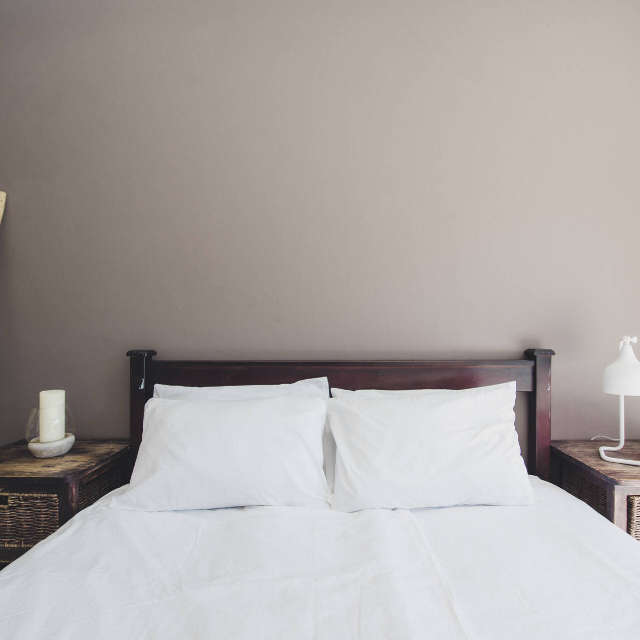 Rustic and cozy poolside double room at Cape Town Surfers Lodge with a double bed, wicker bedside tables, a white lamp, and a wooden towel ladder against a beige wall.