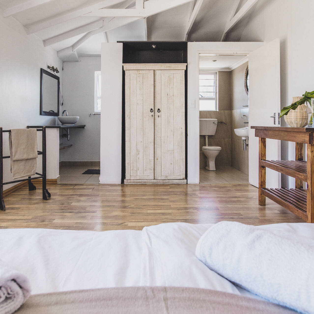 Spacious master bedroom with ensuite bathroom in the poolside apartment at Cape Town Surfers Lodge, featuring rustic wooden furniture and natural light.