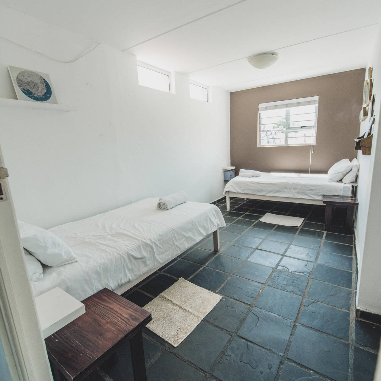 Twin room in the poolside apartment at Cape Town Surfers Lodge with two single beds, white linens, a neutral color palette, and natural light from the window.