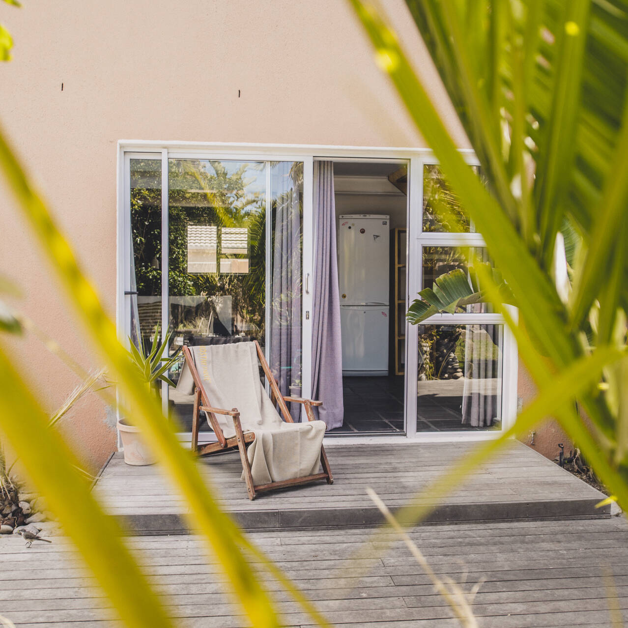 Outdoor patio at the poolside apartment of Cape Town Surfers Lodge with a deck chair, sliding glass doors, and lush greenery.