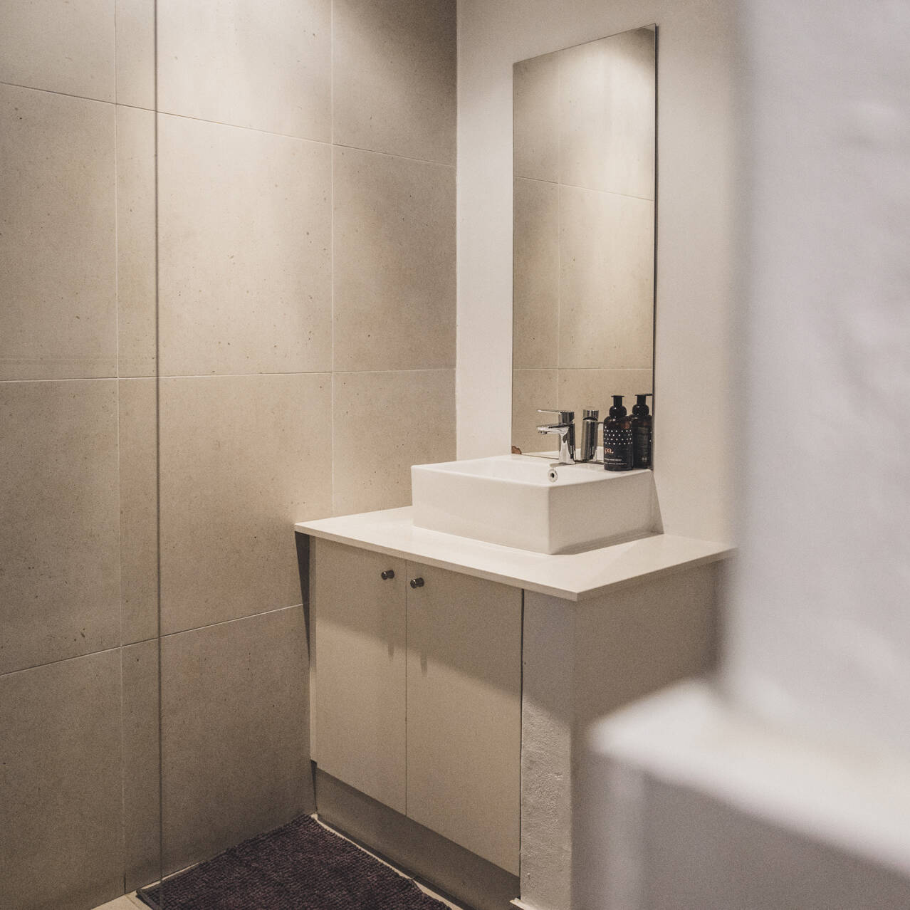 Modern bathroom in the Premium Double Room atCape Town Surfers Lodge with beige tiles, a white countertop sink, and stylish toiletries.