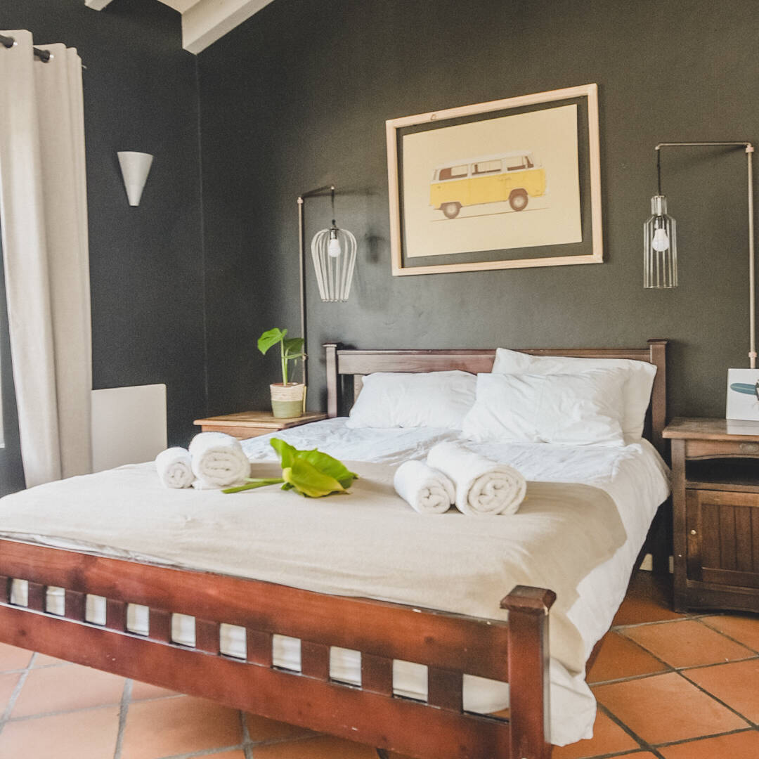 Inviting Premium Double Room at Cape Town Surfers Lodge with a double bed, minimalist bedside tables, modern pendant lighting, and a large window providing natural light. The room includes an artwork of a yellow van.