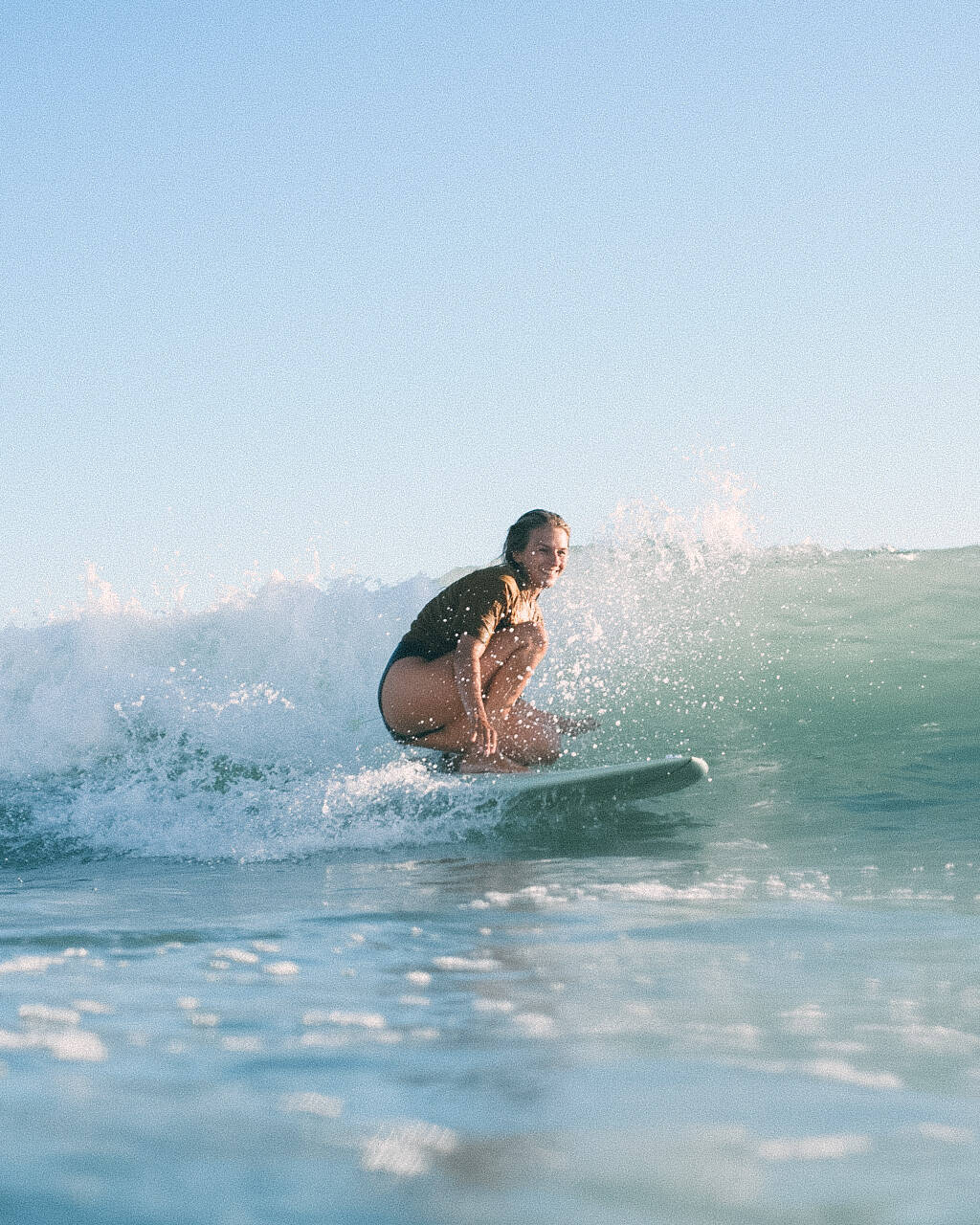 Emely, one of the hosts, riding a wave on her surfboard at Big Bay beach in Cape Town, under a clear blue sky.