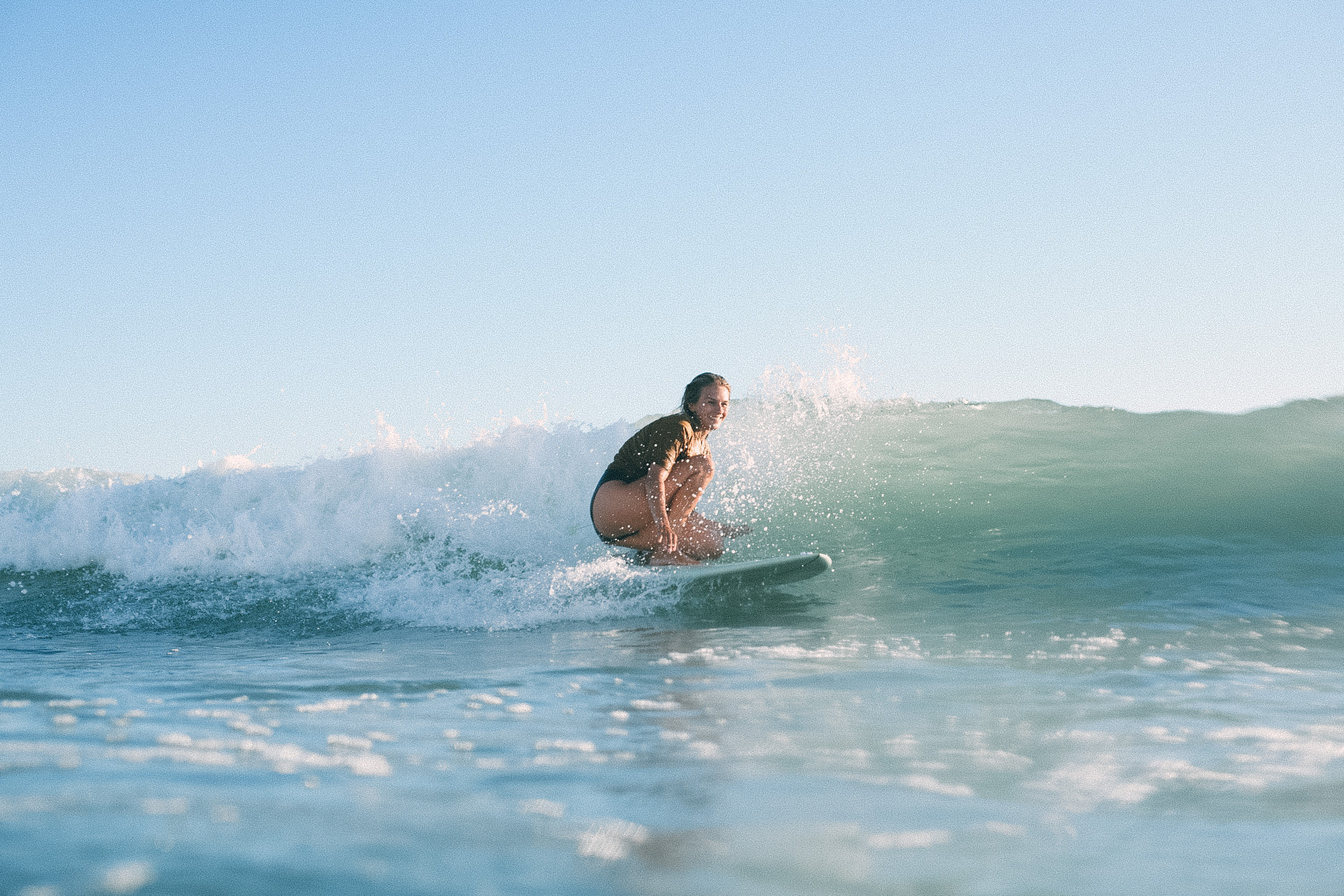 Emely, one of the hosts, riding a wave on her surfboard at Big Bay beach in Cape Town, under a clear blue sky.