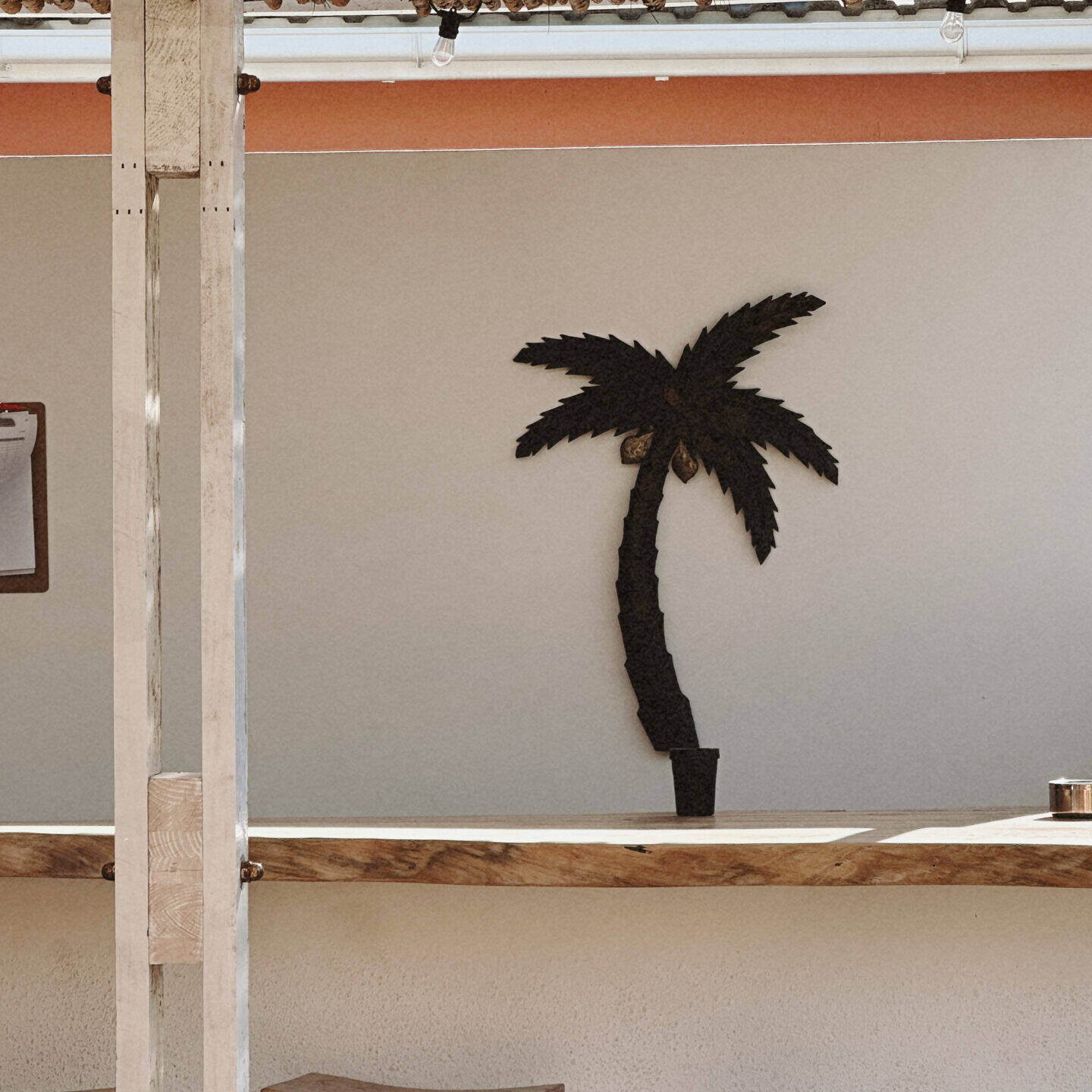 Outdoor pool bar with a wooden counter and stools, shaded by a rustic canopy of wooden slats. A decorative palm tree on the wall adds a tropical touch, creating a cozy and inviting atmosphere.