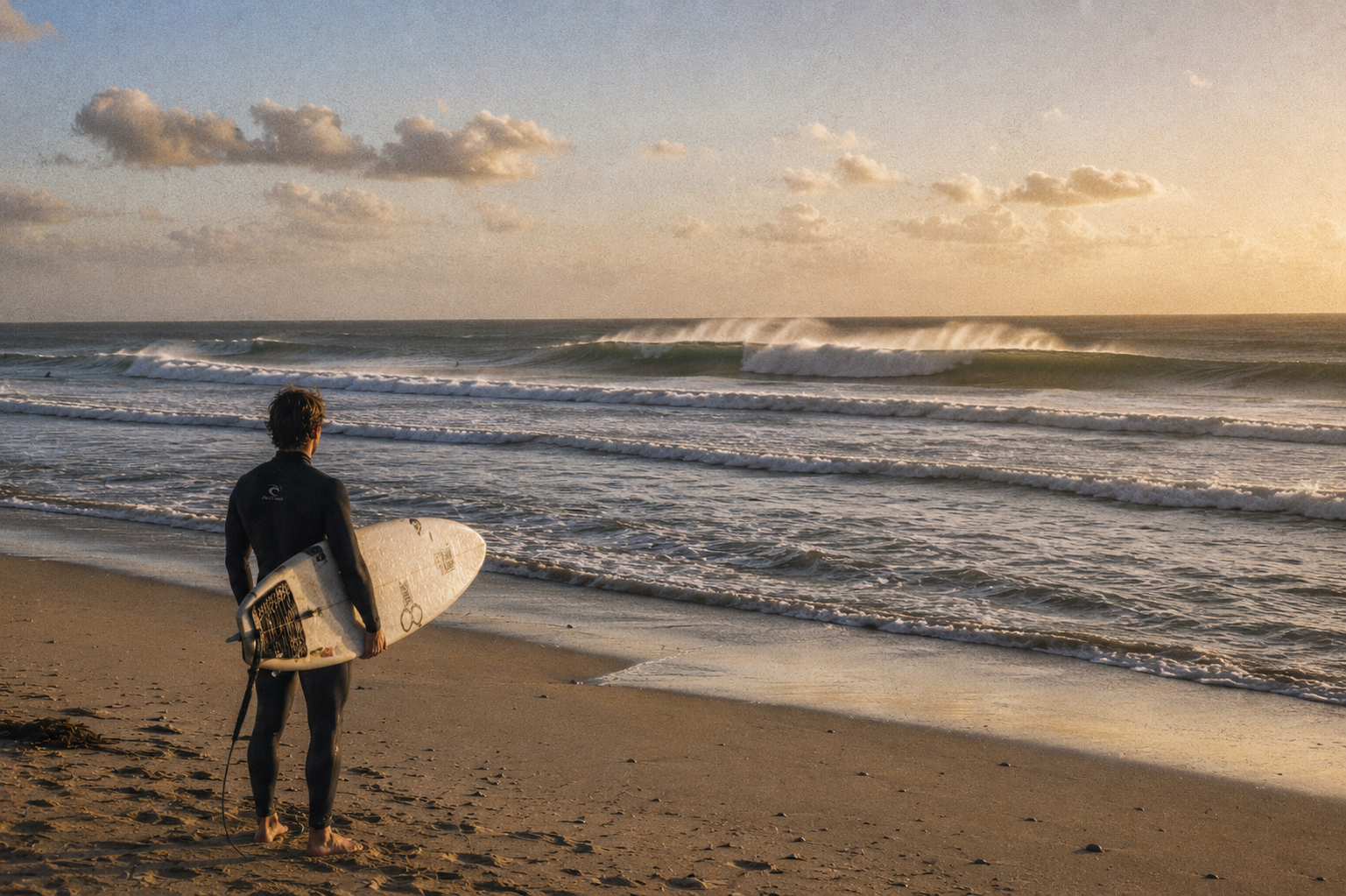 Surfer watching clean winter groundswell at Blouberg Beach in Cape Town during golden hour